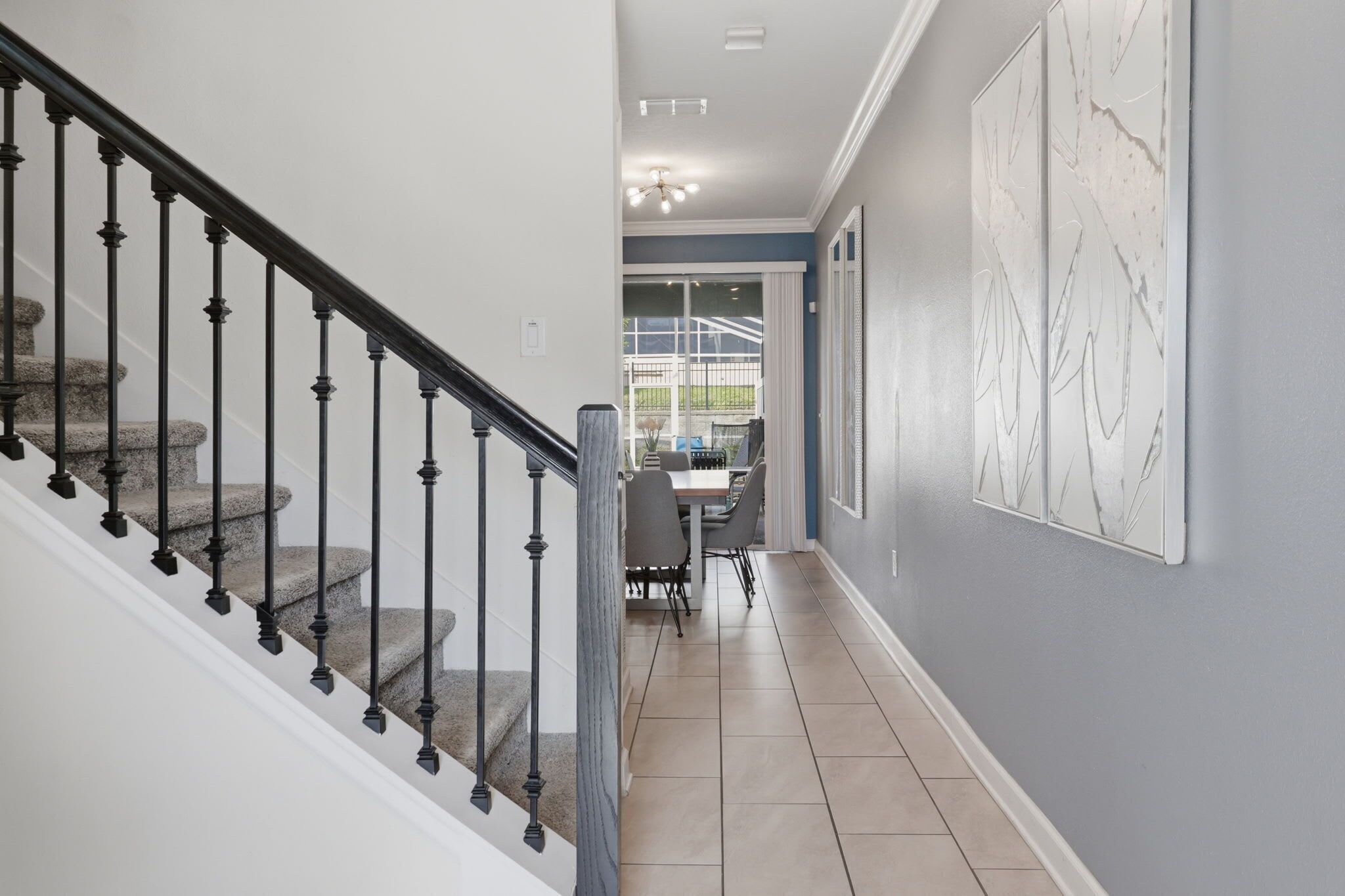 A hallway with a staircase, a dining area with chairs, and a wall with abstract art.