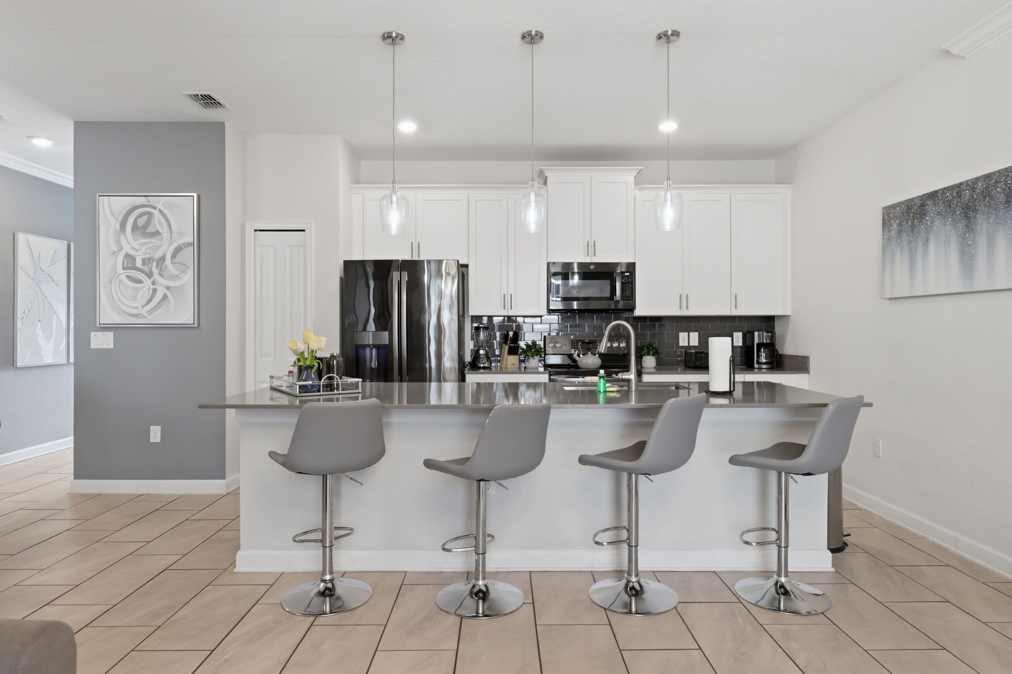 Een moderne keuken met een centraal eiland, barkrukken, roestvrijstalen apparatuur en hanglampen.