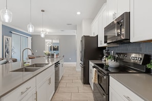 A modern kitchen with stainless steel appliances, a central island, and pendant lighting. - Spacious Champions Gate Townhome - Splash Pool - Walk to Resort - Near Disney (Kissimmee)