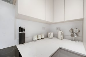 A kitchen with white cabinets, a black knife holder, a toaster, a kettle, and a mug rack. - 2-Bed with Balcony in Northfields -Apt 2 (London)