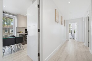 Een moderne keuken met een ingebouwde wasmachine, een eethoek met een zwarte stoel, en een gang met een deur naar een andere kamer.