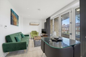 A modern living room with a green sofa, a glass coffee table, and a television. - 2-Bed with Balcony in Northfields -Apt 2 (London)