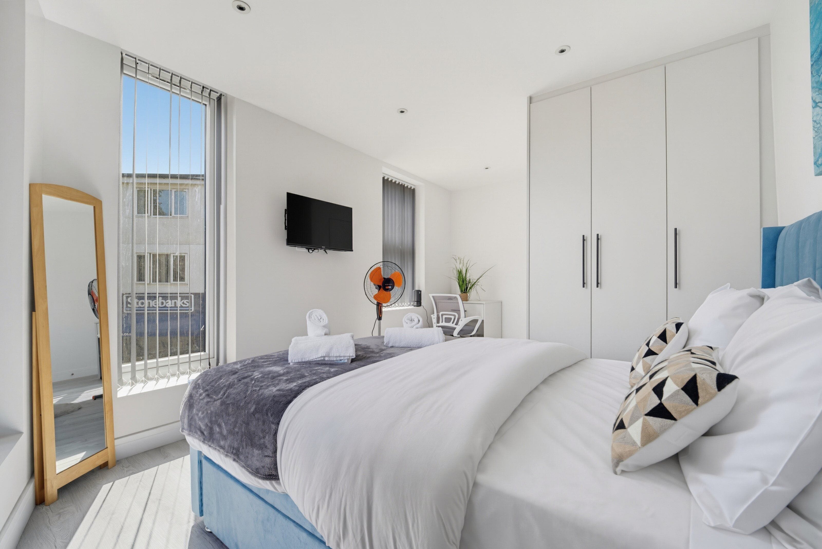 Een moderne slaapkamer met een bed, een televisie, een spiegel en een raam met zonwering.