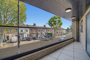 A balcony with a view of a residential street, featuring parked cars and houses. - 2-Bed with Balcony in Northfields -Apt 2 (London)