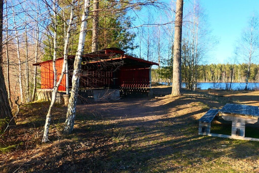 A cabin with a red exterior, surrounded by trees and a body of water.