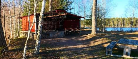 A cabin with a red exterior, surrounded by trees and a body of water.