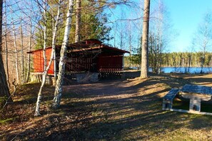 A cabin with a red exterior, surrounded by trees and a body of water. - Holiday home in Vimmerby with swimming pool (Vimmerby)