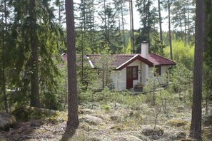 Eine kleine Holzhütte mit rotem Dach, umgeben von dichtem Wald.