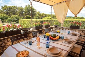 An outdoor dining area with a table set for two, surrounded by stone walls and potted plants.