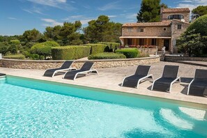 A swimming pool with lounge chairs and a stone building with a tiled roof.