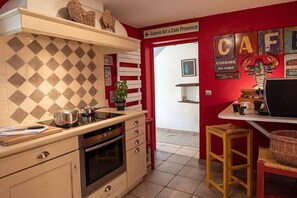 A kitchen with a tiled backsplash, a stove, and a sink. There is a red wall with a sign that reads 'Galerie Art & Com Provence.' - Cabin in Ménerbes with swimming pool (Ménerbes)