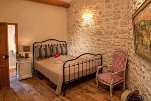 Ein Schlafzimmer mit Stehwand, einem Bett mit Metallgestell, einem Stuhl und einem Nachttischchen mit Lampe.