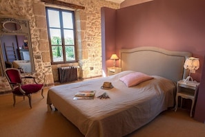 Ein Schlafzimmer mit Steinsturz, großem Fenster, Bett mit Kopfteil, Stuhl und Nachttisch mit Lampe.