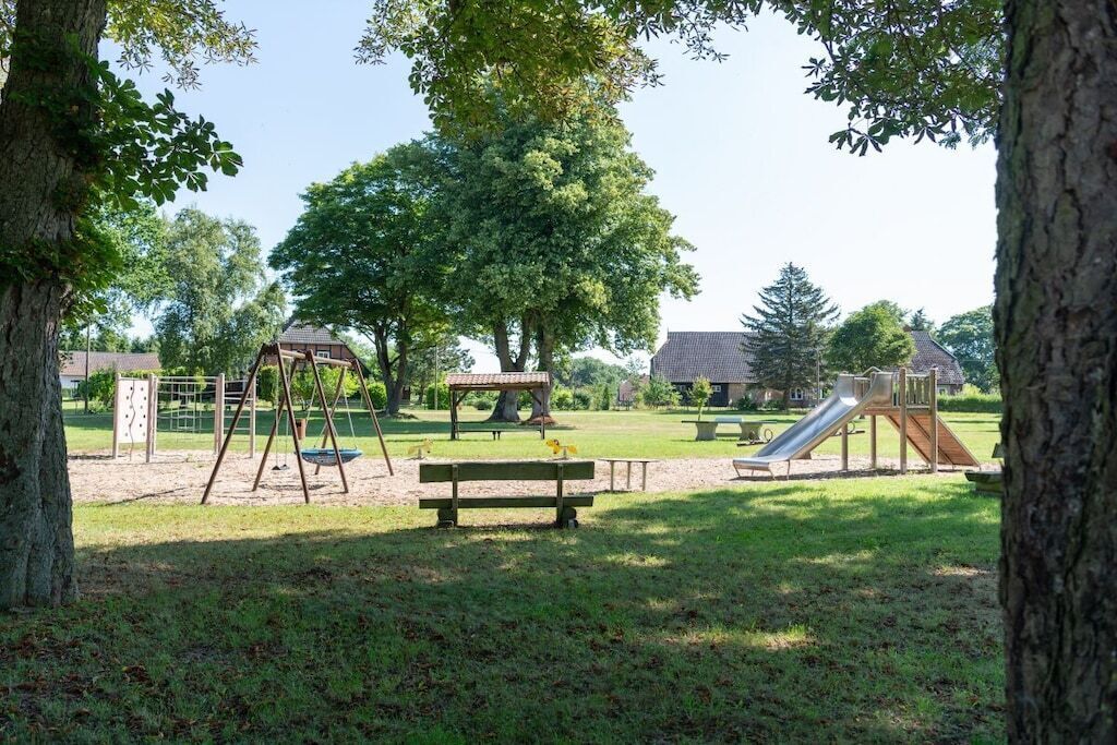 A park with playground equipment, a picnic table, and a large tree.