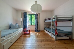 Et værelse med køjeseng, enkeltseng, et lille bord og et vindue med gardiner.