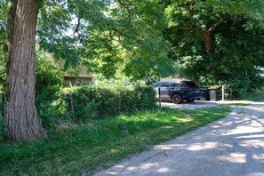 A car parked on a gravel path beside a tree, with a building in the background. - Under the starry sky (Reimershagen)