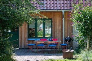 An outdoor patio with a wooden table and blue chairs, a grill, and a green door. - Under the starry sky (Reimershagen)
