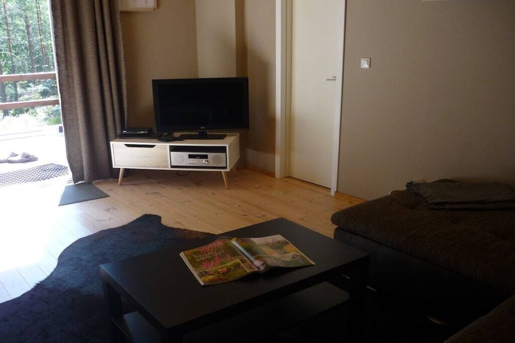 Une pièce avec un téléviseur posé sur un meuble, une petite table avec un magazine, un canapé et une porte.