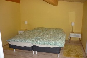 Un llit individual amb un estovat estampat, dues taules de nit i una catifa petita sobre un terra de fusta.