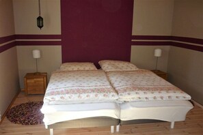 Un lit double avec une literie à motifs floraux, deux tables de chevet, une lampe suspendue et un tapis à motifs.