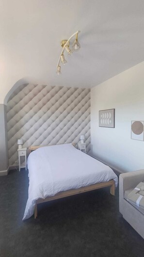 Ein Schlafzimmer mit einem Bett, Nachttischen, einer Wandleuchte und einem Sofa.
