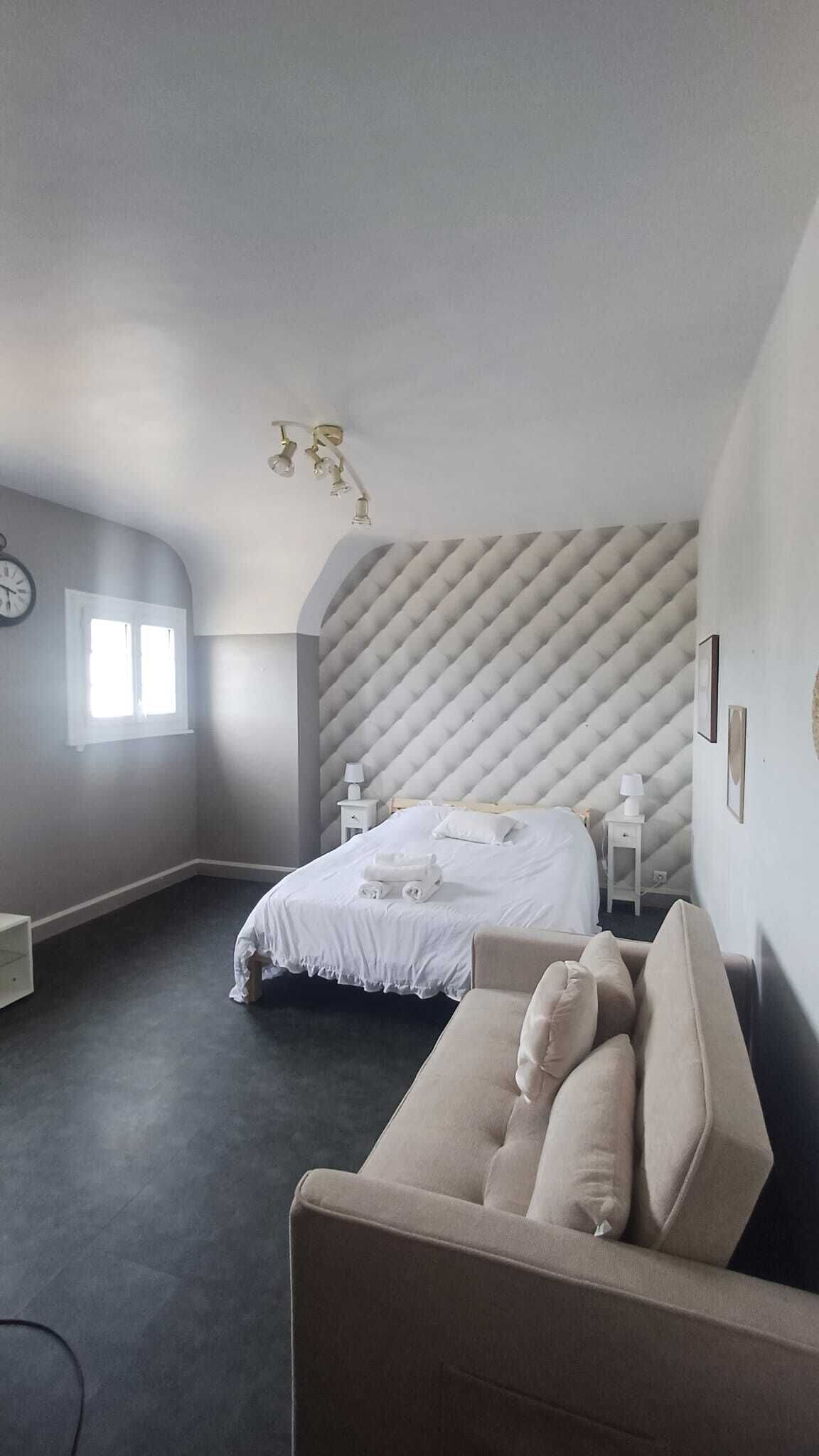 A bedroom with a bed, a sofa, a nightstand, a wall clock, and a window.