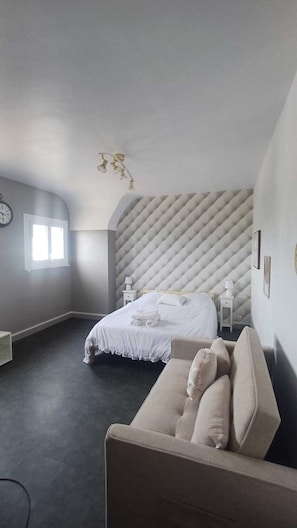 Ein Schlafzimmer mit einem Bett, einem Sofa, einem Nachttisch, einer Wanduhr und einem Fenster.