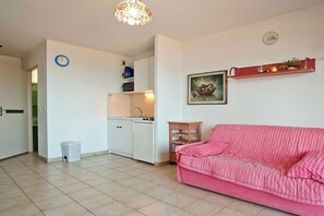 A compact living space with a kitchenette, a pink sofa, a clock, and a framed picture on the wall. - Holiday apartment with 1 bedroom (Saint-Florent)