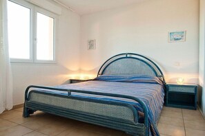 A single bed with a metal frame and a headboard, two bedside tables, and a window with curtains. - Holiday apartment with 1 bedroom (Saint-Florent)