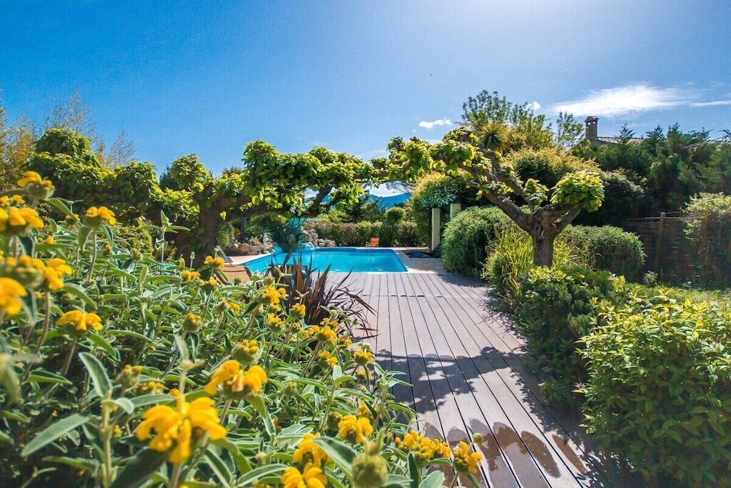 A wooden deck leading to a swimming pool surrounded by lush greenery and trees.