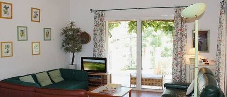 Una sala de estar con un sofá verde, un televisor, una mesa de centro y una planta.