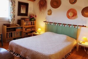 Une chambre à coucher avec un lit, une table de chevet avec une lampe, une bibliothèque et un mur décoré de chapeaux.