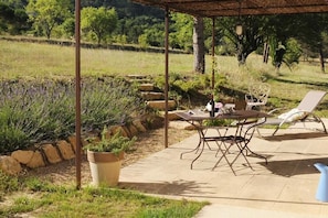 An outdoor patio with a table and chairs, surrounded by a garden with a stone wall and trees. - Holiday apartment in Apt with swimming pool (Apt)
