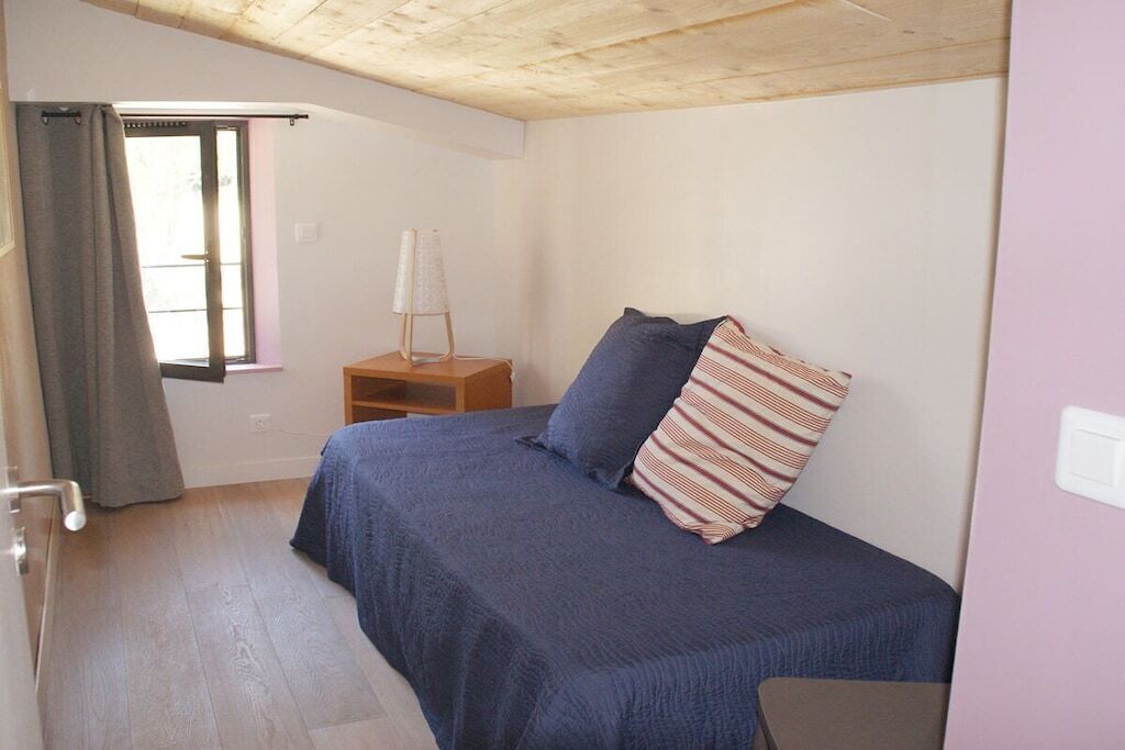 A bedroom with a bed, a nightstand, a lamp, and a window with curtains.