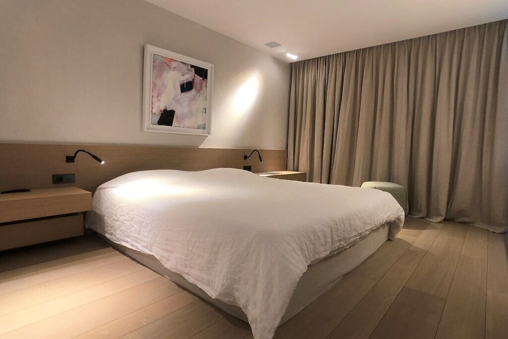 A modern hotel room with a large bed, bedside tables, a wall-mounted light, and a window with curtains.