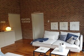 A room with a brick wall, white sofa, and a small table with a lamp. - Holiday home with 2 bedrooms (Retranchement)