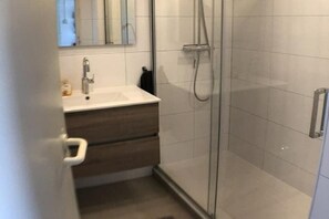 A bathroom with a glass-enclosed shower, a white sink, and a wooden vanity. - Holiday home with 2 bedrooms (Retranchement)