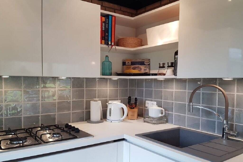 Eine moderne Küche mit Gasherd, Spüle und einer Arbeitsplatte mit verschiedenen Gegenständen, darunter ein Wasserkocher, eine Kaffeemaschine und eine Teedose.