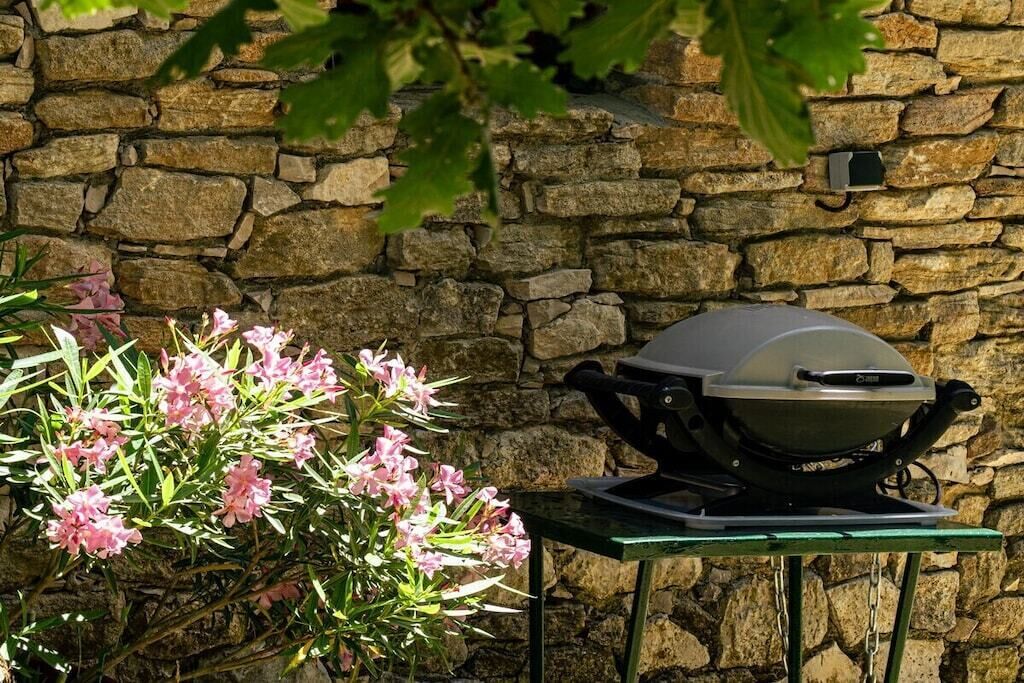A stone wall, a grill on a table, and pink flowers.
