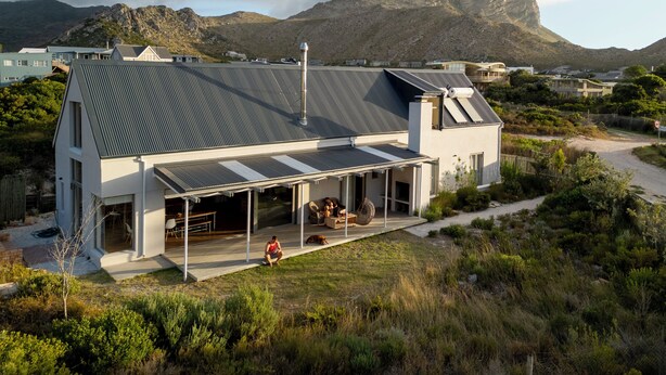 Une maison moderne dotée d’un grand patio, d’un espace salon extérieur couvert et offrant une vue sur les montagnes en arrière-plan.