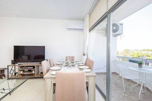 A dining area with a table set for four, a television, and a balcony with a table and chairs. - Artemis Salt Lake 3BR Apartment Mackenzie (Larnaka)