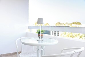 Een ronde tafel met een bloempot en een lamp op een balkon met een witte reling en uitzicht op bomen.