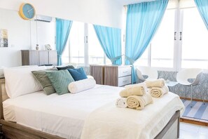 A hotel room with a bed, a nightstand, a chair, and a window with curtains. - Artemis Salt Lake 3BR Apartment Mackenzie (Larnaka)