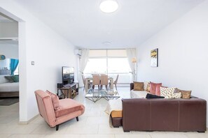 A modern living room with a sofa, armchair, and a TV on a stand. - Artemis Salt Lake 3BR Apartment Mackenzie (Larnaka)