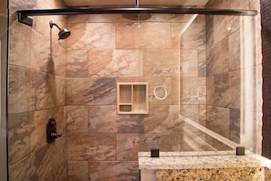 Une douche avec un espace clos en verre, une douchette à main et un panneau de commande fixé au mur.