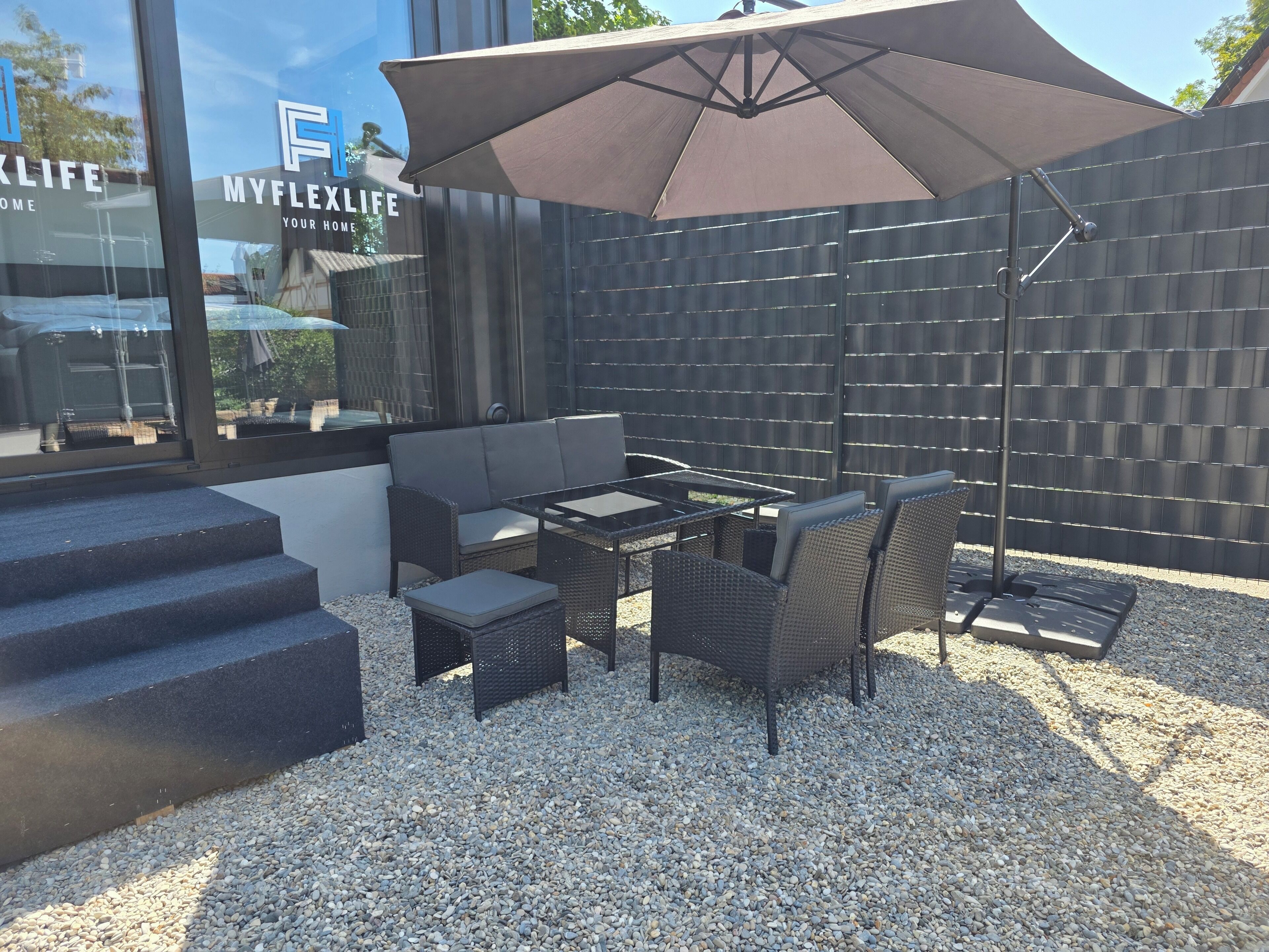 Un espace extérieur aménagé avec un canapé, une table, des chaises et un grand parasol.