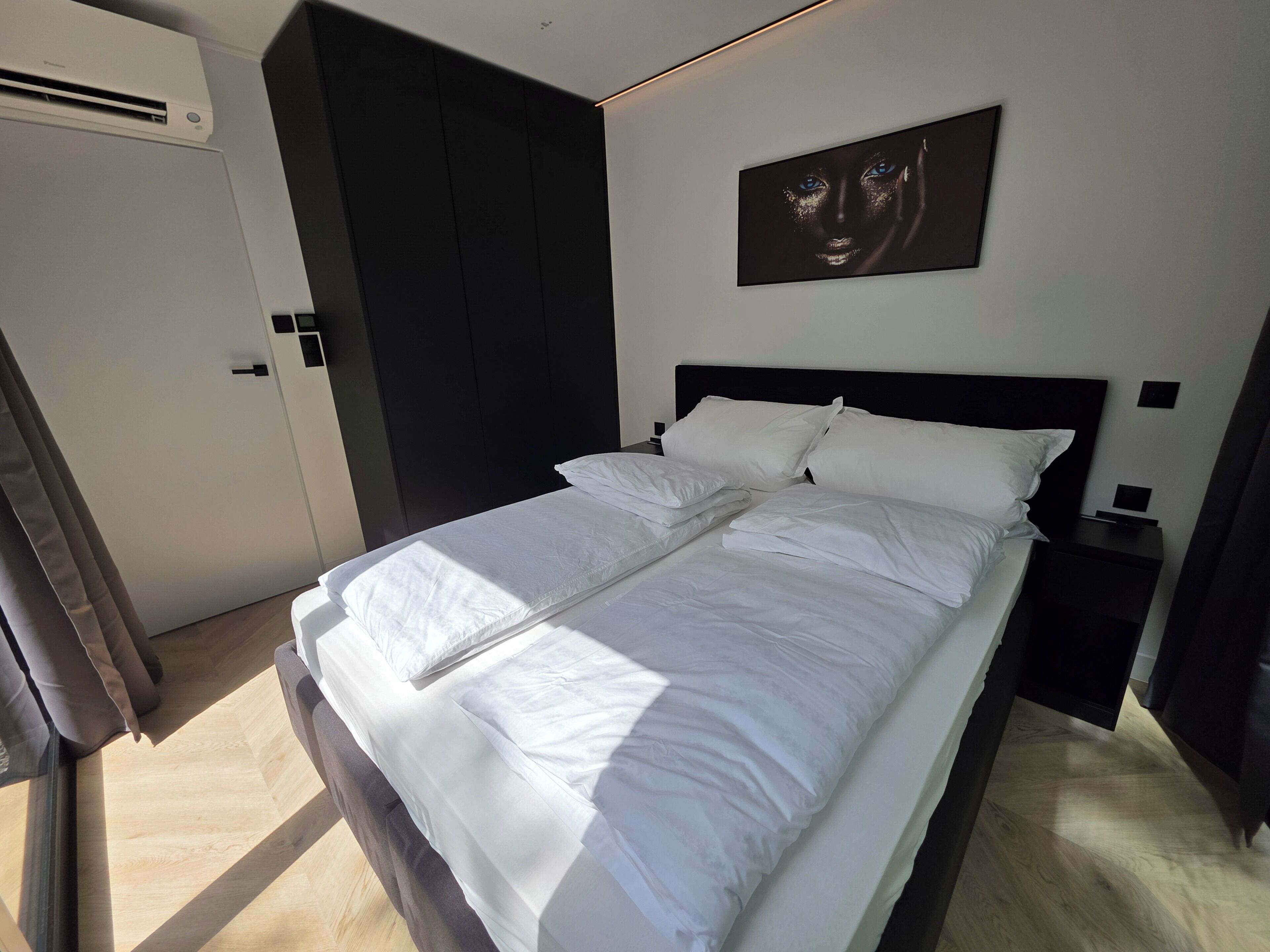 Une chambre d’hôtel moderne avec un grand lit, une tête de lit sombre, une œuvre d’art accrochée au mur et une table de chevet avec une lampe.