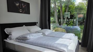 Ein modernes Schlafzimmer mit einem großen Bett, einer Kopfteil und einem Fenster mit Blick auf Bäume und ein Gebäude.