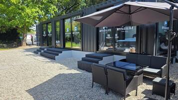 Ein Außenbereich zum Sitzen mit modernem Design, ausgestattet mit einer Glasfassade, Gartenmöbeln und einer Pergola.