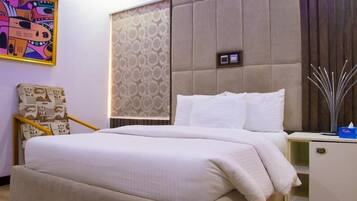 Quarto de hotel com cama, mesa de cabeceira, cadeira e parede com papel de parede estampado e um quadro emoldurado.